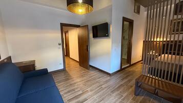Ein modernes Wohnzimmer mit einem blauen Sofa, Holzboden, einem an der Wand montierten Fernseher und einer Treppe mit Geländer.
