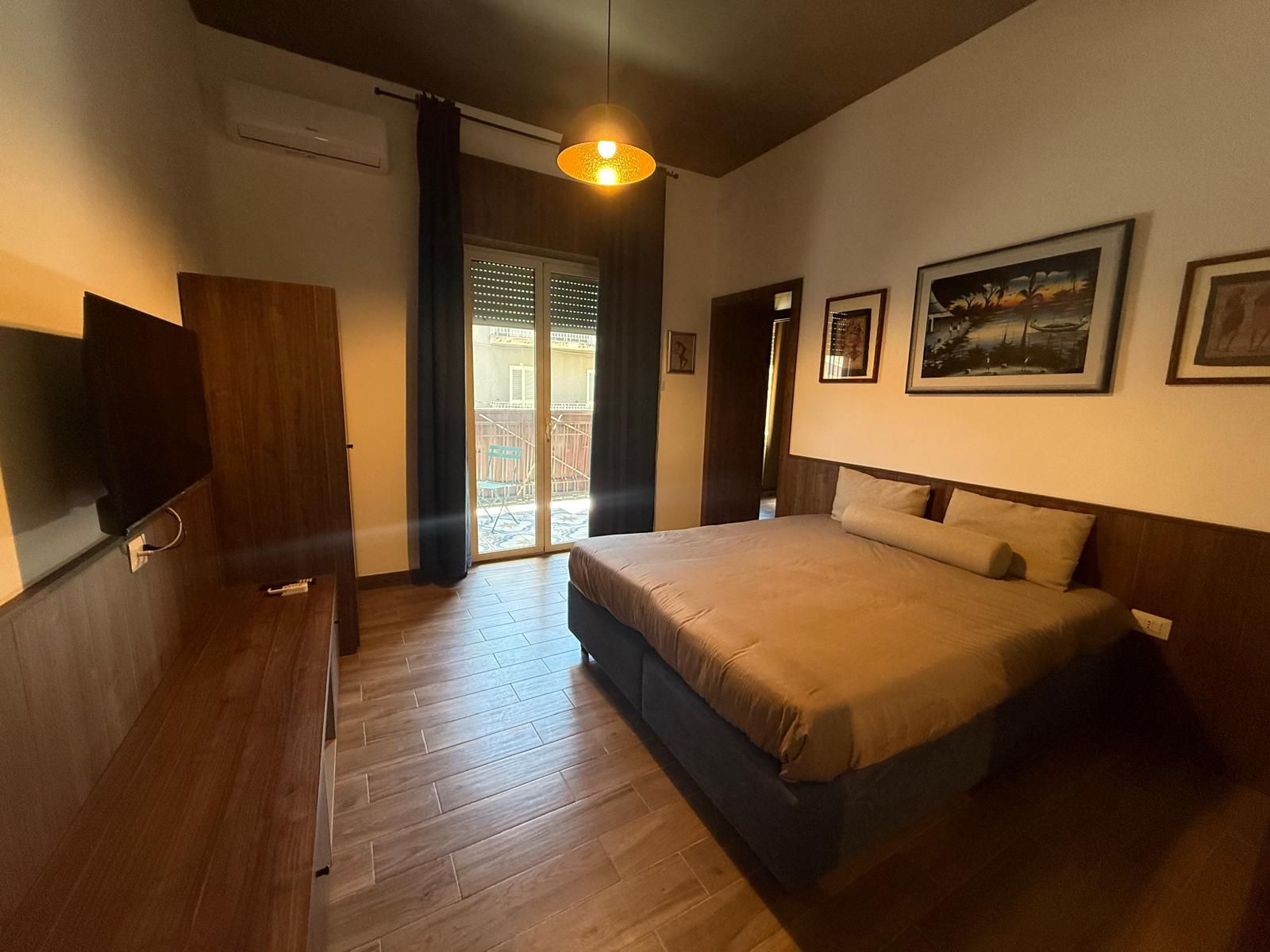 A bedroom with a bed, a television, and a sliding glass door leading to a balcony.
