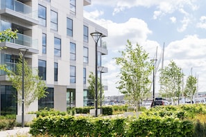 Een modern gebouw met meerdere verdiepingen, grote ramen en een aangelegde omgeving met bomen en struiken.