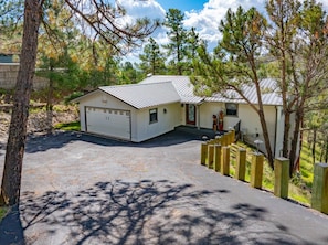A two-story house with a garage, surrounded by trees and a paved driveway. - Mountain Mischief - 4 Suites + Views + Hot Tub (Alto)