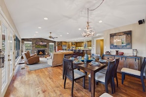 A spacious living area with a fireplace, a dining table set for six, and a kitchen in the background. - Mountain Mischief - 4 Suites + Views + Hot Tub (Alto)