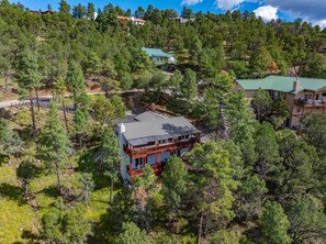A two-story house with a green roof, surrounded by dense pine trees. - Mountain Mischief - 4 Suites + Views + Hot Tub (Alto)