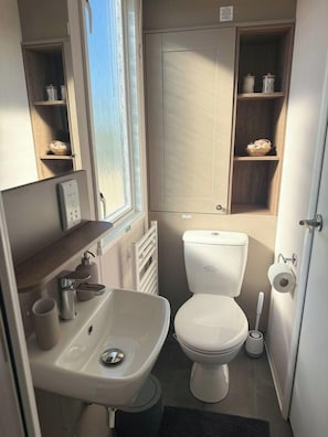 A compact bathroom with a toilet, sink, and storage shelves.