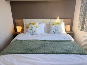 A hotel room with a bed, two bedside lamps, and a green blanket.