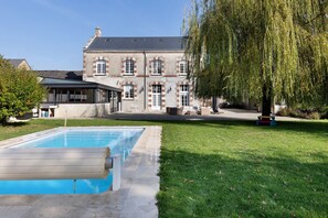 Una casa grande con piscina, un porche cubierto y un césped bien cuidado.