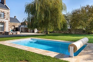 A swimming pool with a stone border, a covered hot tub, and a weeping willow tree. - Holiday Home 'L'appartement Du Manoir' with Private Pool, Private Terrace and Wi-Fi (Moisy)