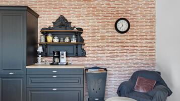A room with a brick wall, a clock, a cabinet, a coffee maker, and a chair.