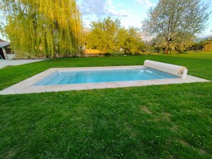 En rektangulär swimmingpool med en vit kant, omgiven av välskött gräs.