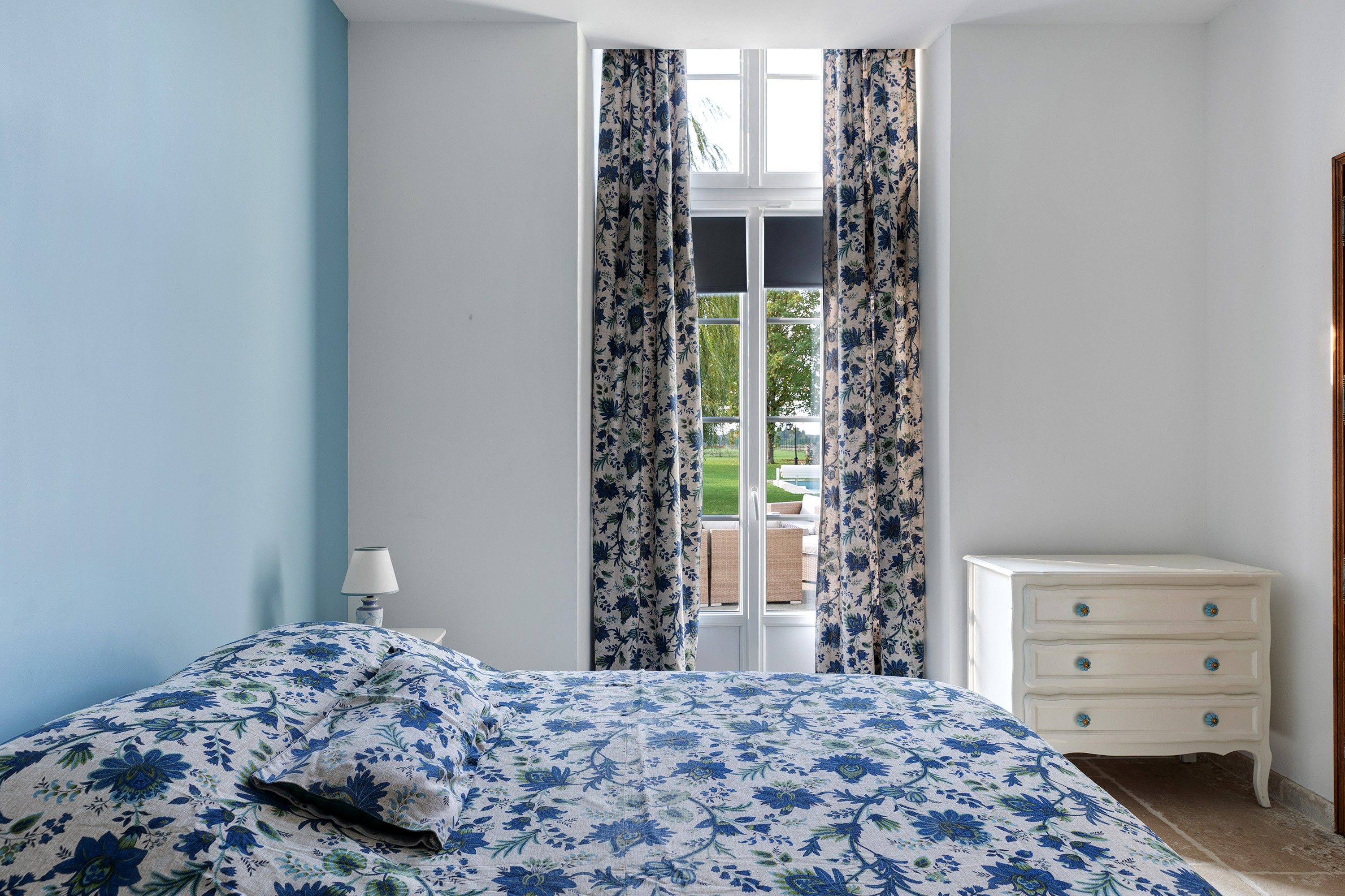 A bedroom with a bed, a nightstand, a dresser, and a window with curtains.