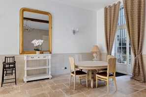 A room with a round table, two chairs, a white console with a mirror, a lamp, and a window with curtains. - Holiday Home 'L'appartement Du Manoir' with Private Pool, Private Terrace and Wi-Fi (Moisy)