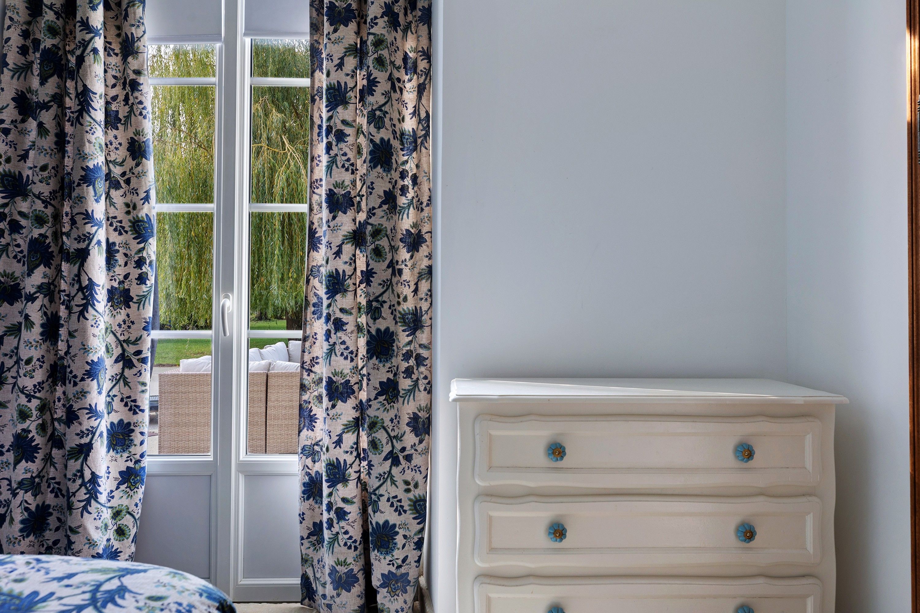 A bedroom with a window, white dresser, and floral curtains.