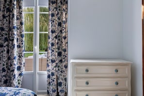 A bedroom with a window, white dresser, and floral curtains.