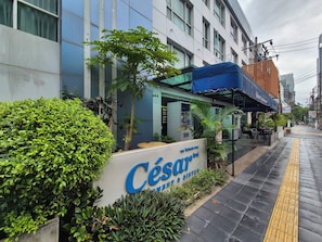 Entrada de un hotel con un letrero que dice 'César Hotel & Restaurant' y un área de estar al aire libre techada.