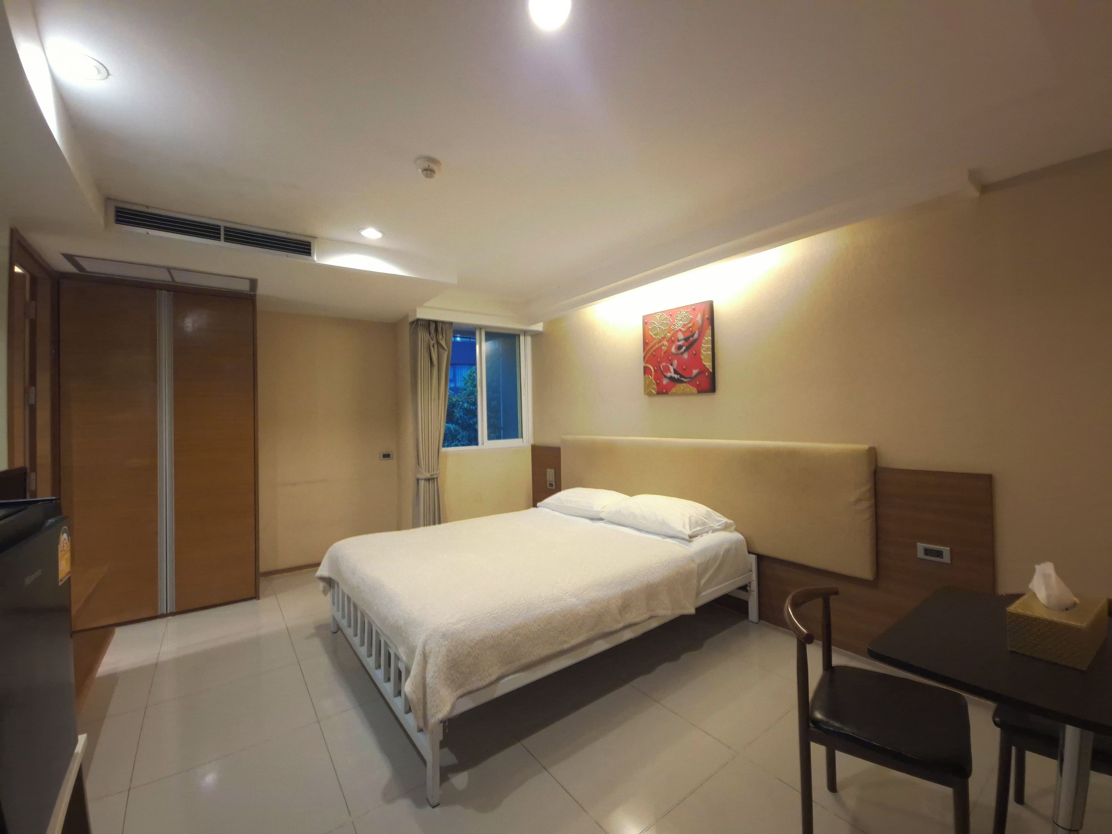 Ein Hotelzimmer mit einem Bett, einem Schreibtisch, einem Stuhl, einem Fenster mit Vorhängen und einem an der Wand hängenden Kunstwerk.