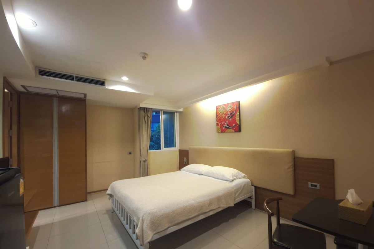 A hotel room with a bed, a desk, a chair, a window with curtains, and a wall-mounted artwork.