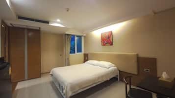 A hotel room with a bed, a desk, a chair, a window with curtains, and a wall-mounted artwork.