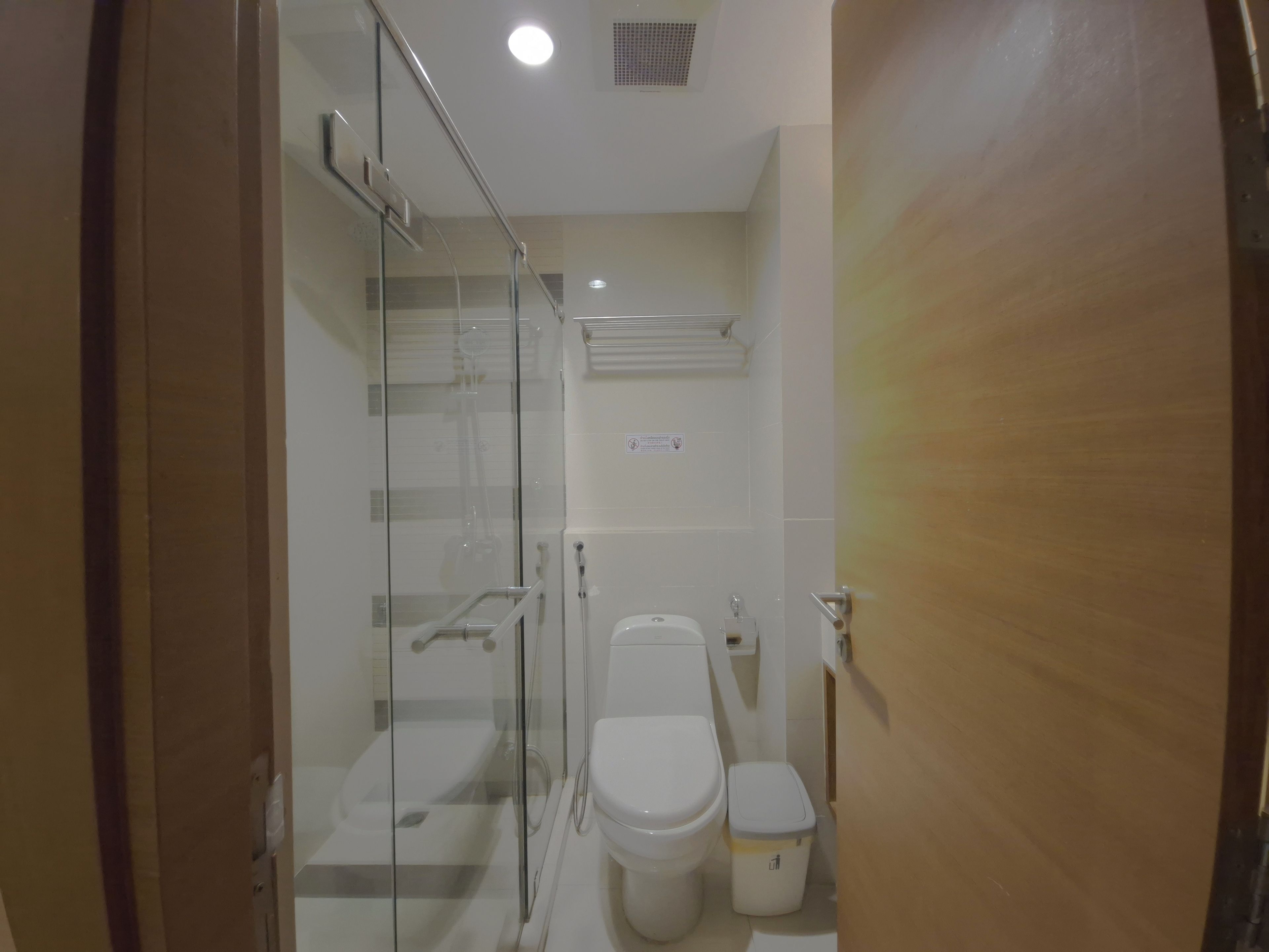 A bathroom with a glass-enclosed shower, a toilet, and a trash bin.