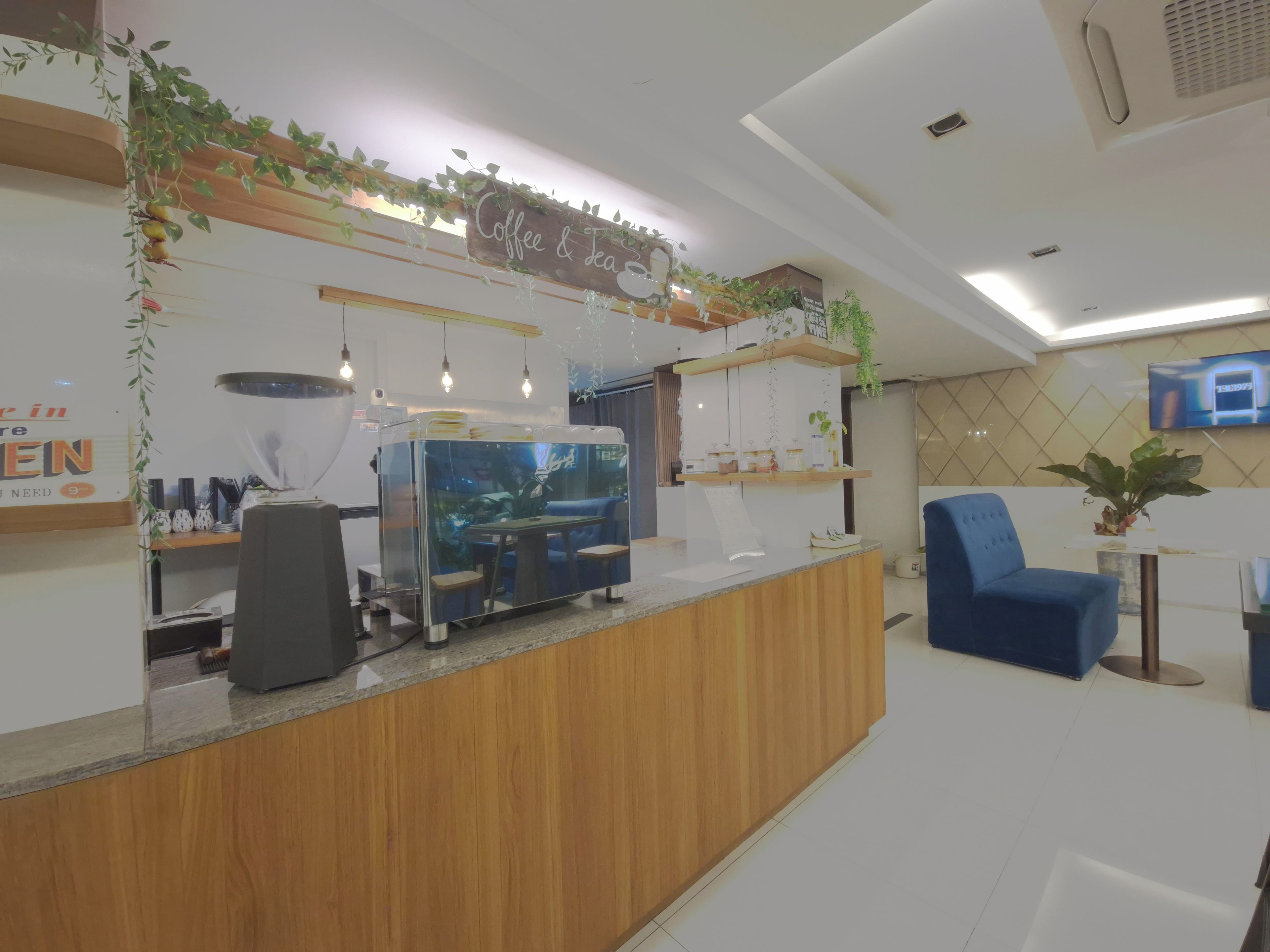 A reception area with a wooden counter, a coffee machine, and a seating area with a blue chair.