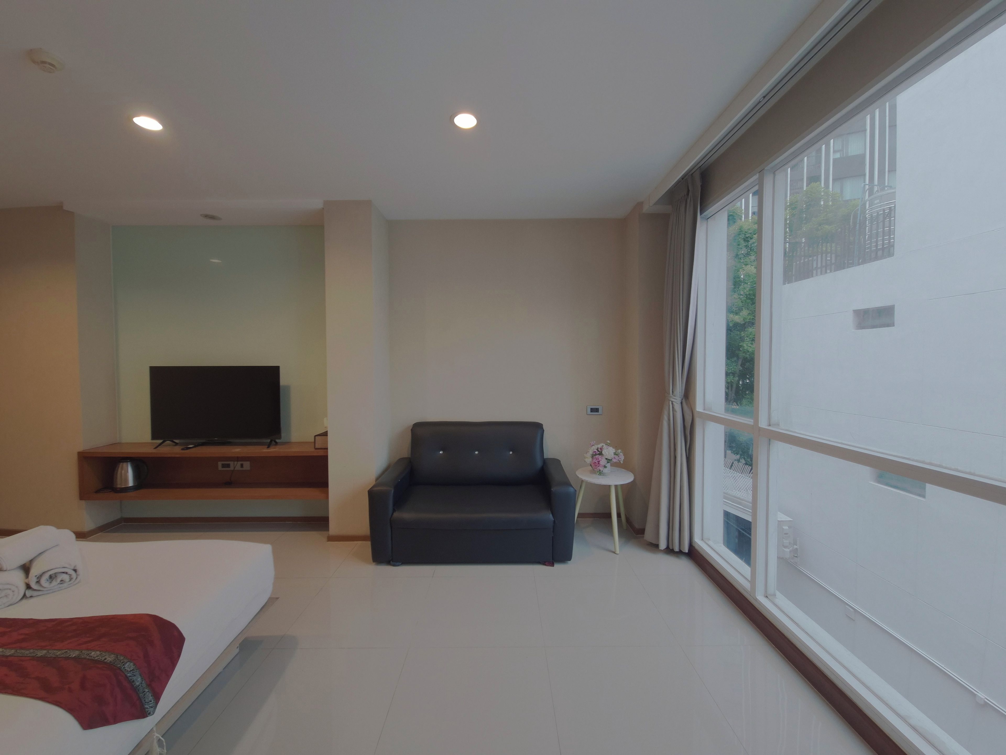 Una habitación de hotel con cama, televisor, sofá y ventana con cortinas.