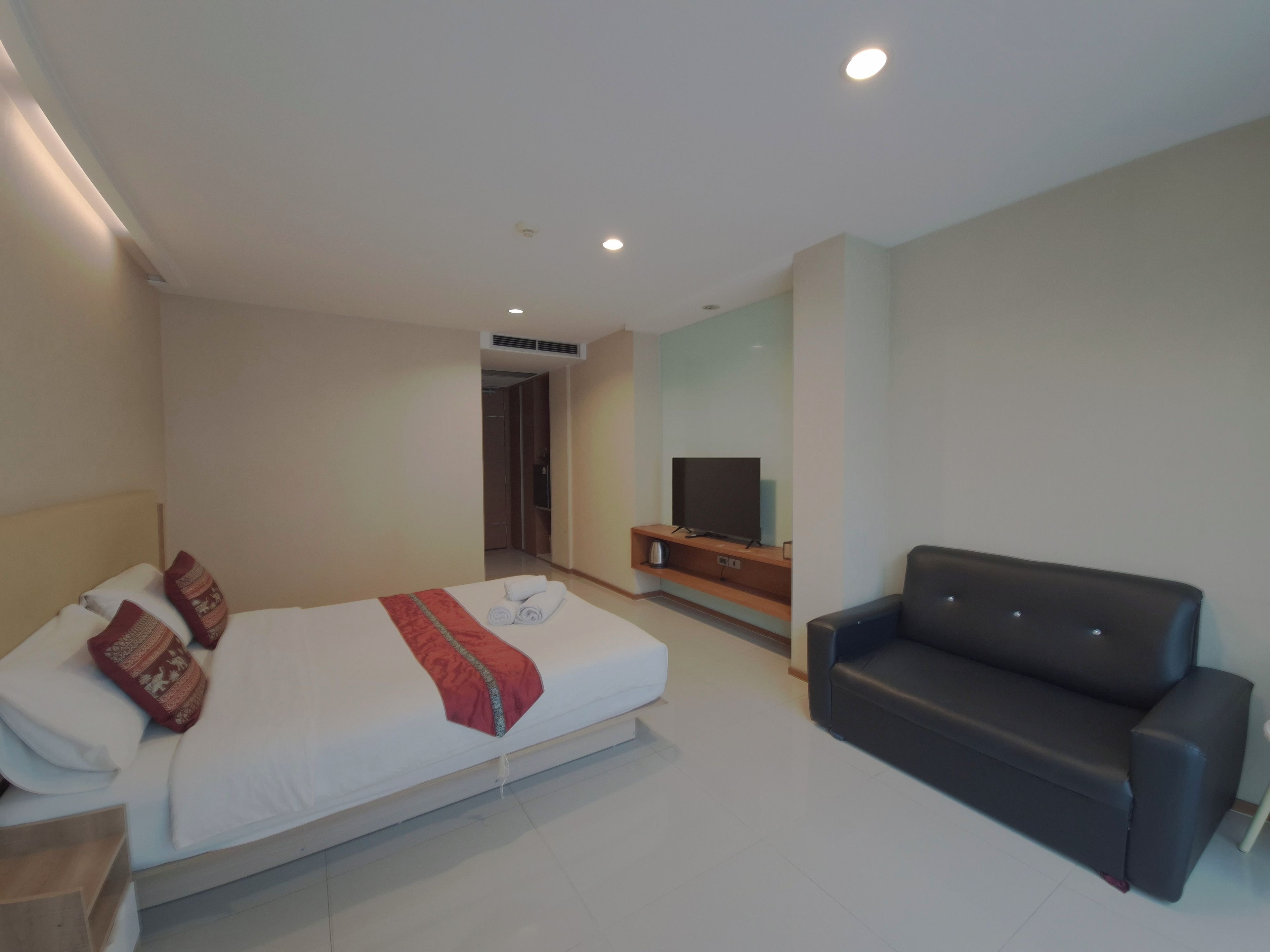 Quarto de hotel moderno com cama, televisão de tela plana, sofá e closet espaçoso.