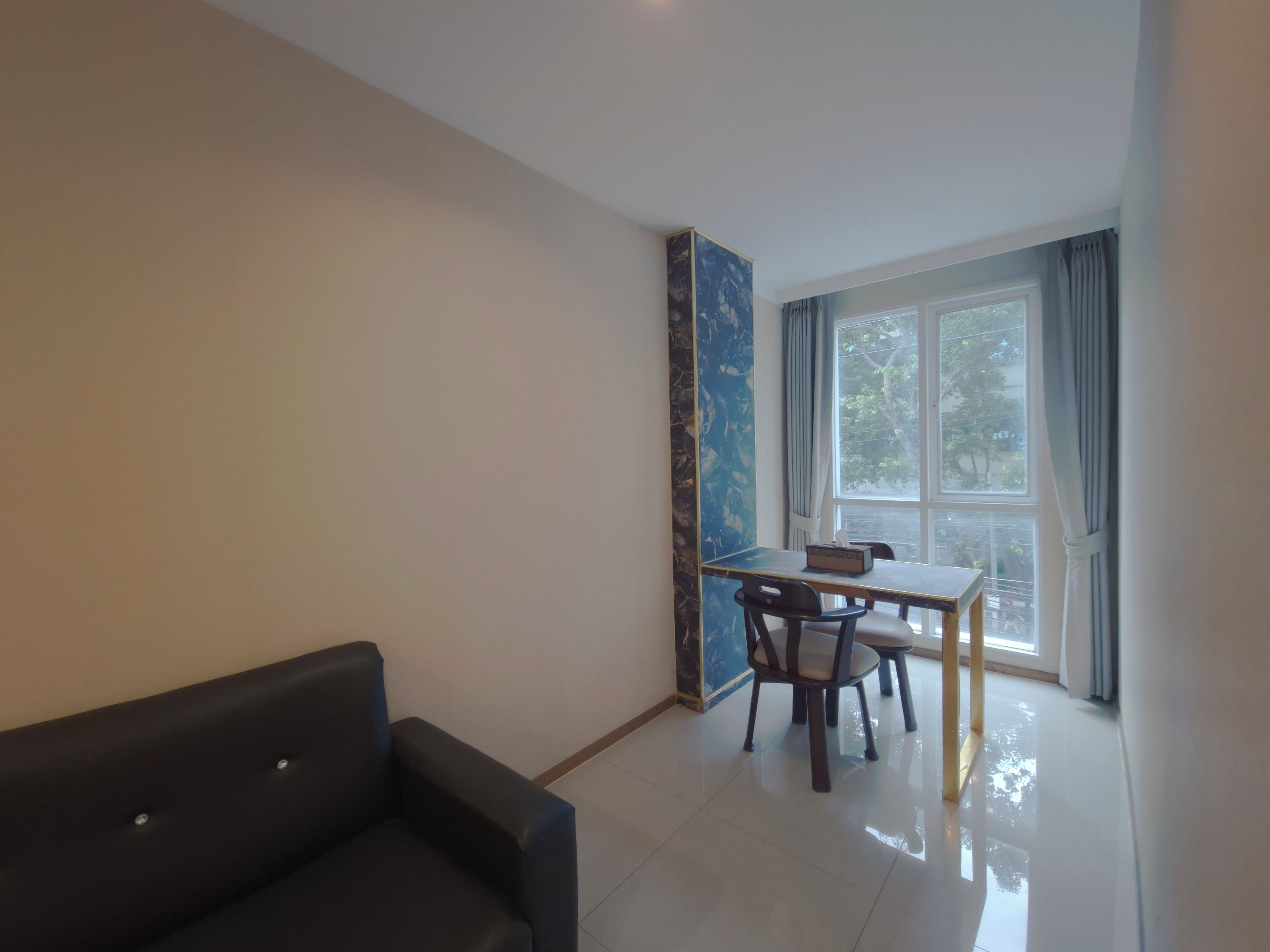 Una habitación con sofá, una mesa y sillas, una ventana con cortinas y una pared con diseño abstracto azul.