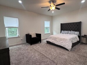 Ein Schlafzimmer mit einem Bett, einem Sessel, einem Deckenventilator und zwei Fenstern.