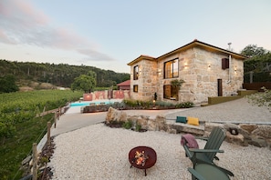 Una casa de piedra con piscina, rodeada por un patio de grava y un viñedo.