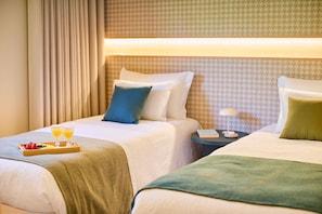 Habitación de hotel con dos camas, una bandeja de fruta y jugo, y una mesita de noche con lámpara.