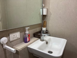 Une salle de bain avec un lavabo blanc, un miroir, un distributeur de savon et une bouteille de savon liquide Dettol pour les mains.