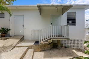 A residential building with a white exterior, a concrete staircase leading to a porch, and a door with a window. - Casa Pueblo Mar: Rincón Town Living with Sunset Sea Views (Rincon)