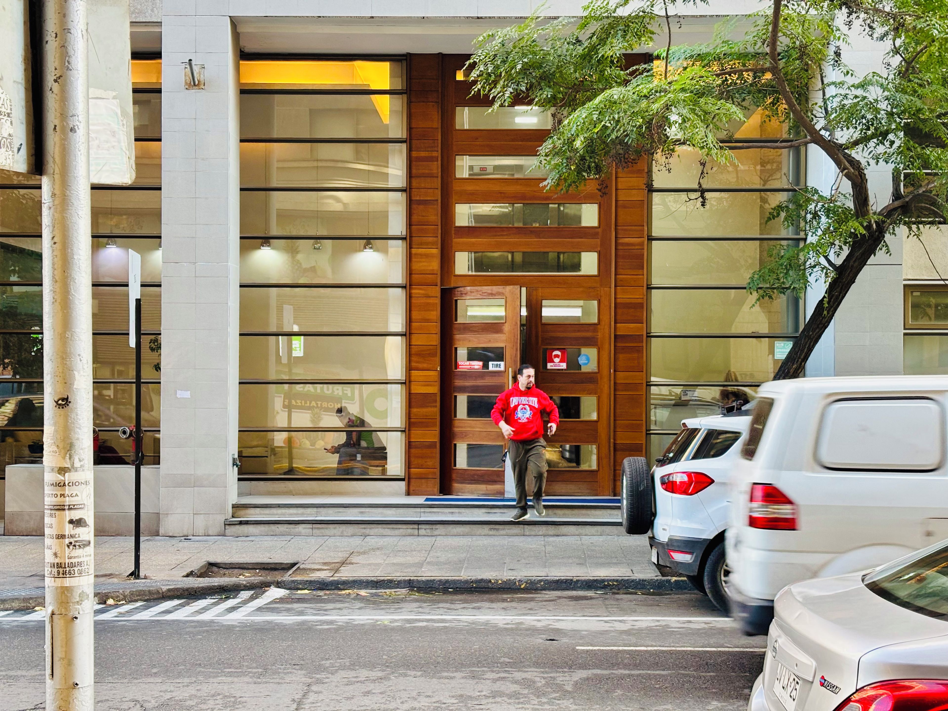 Ein Gebäude mit großen Glasfenstern, einer Holztür und einer Person, die davor entlanggeht.