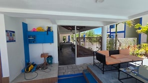 A covered outdoor seating area with a table and chairs, a blue storage unit, and a pathway leading to a building entrance. - Long Beach Laamu (Gan)