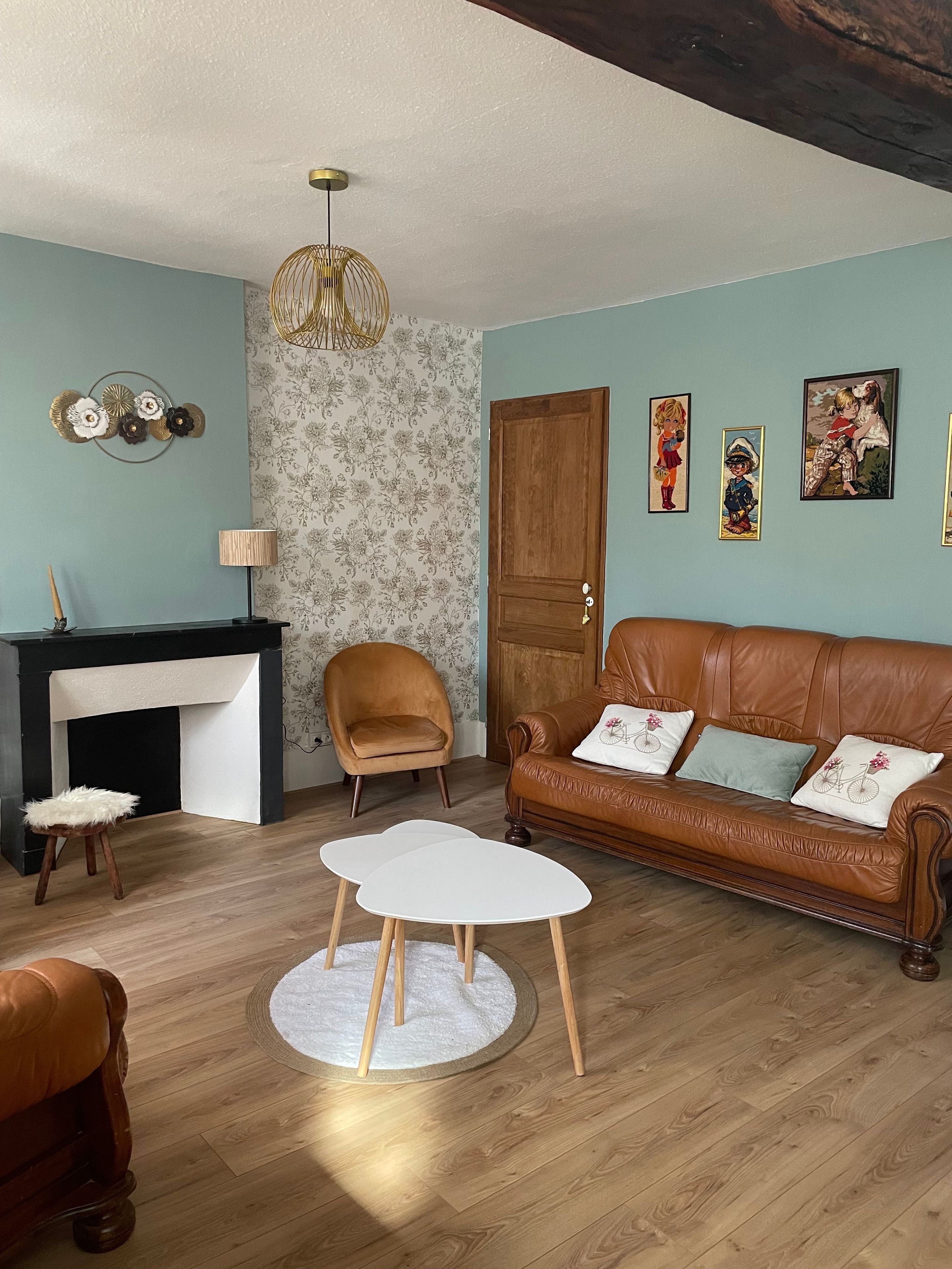 A living room with a fireplace, a brown leather sofa, a round coffee table, a wooden chair, and wall art.