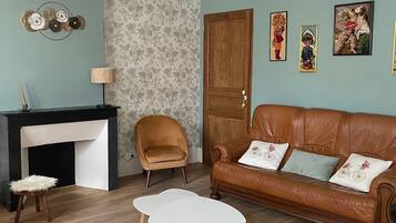 A living room with a fireplace, a brown leather sofa, a round coffee table, a wooden chair, and wall art.