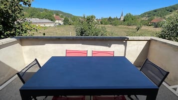 Eine Außenpatio mit Tisch und Stühlen, bewölkter Himmel und Blick auf ein Dorf mit Häusern und einer Kirche.