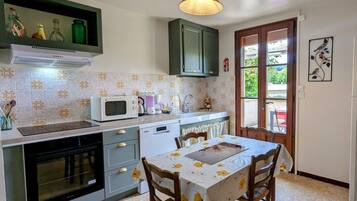 A kitchen with a dining table, a microwave, a dishwasher, and a window with a view of greenery.