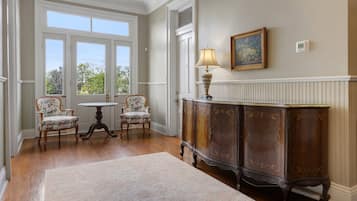 A room with a large window, a wooden cabinet, two chairs, a small table, and a lamp.