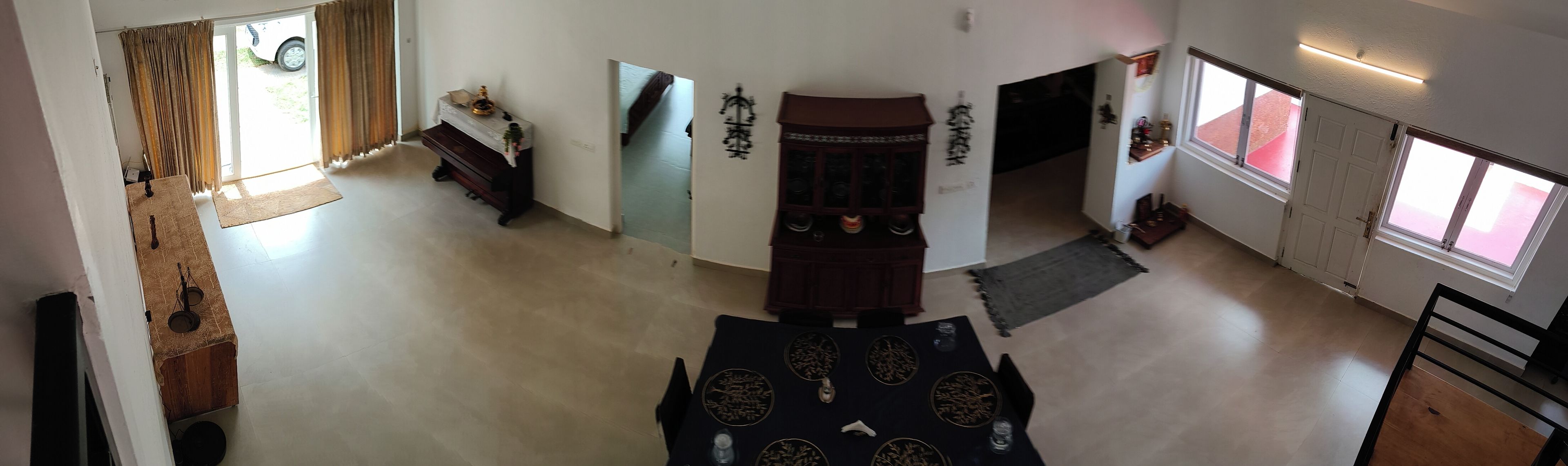 A spacious room with a high ceiling, a dining area with a table set for four, and a view of the outside through a window.