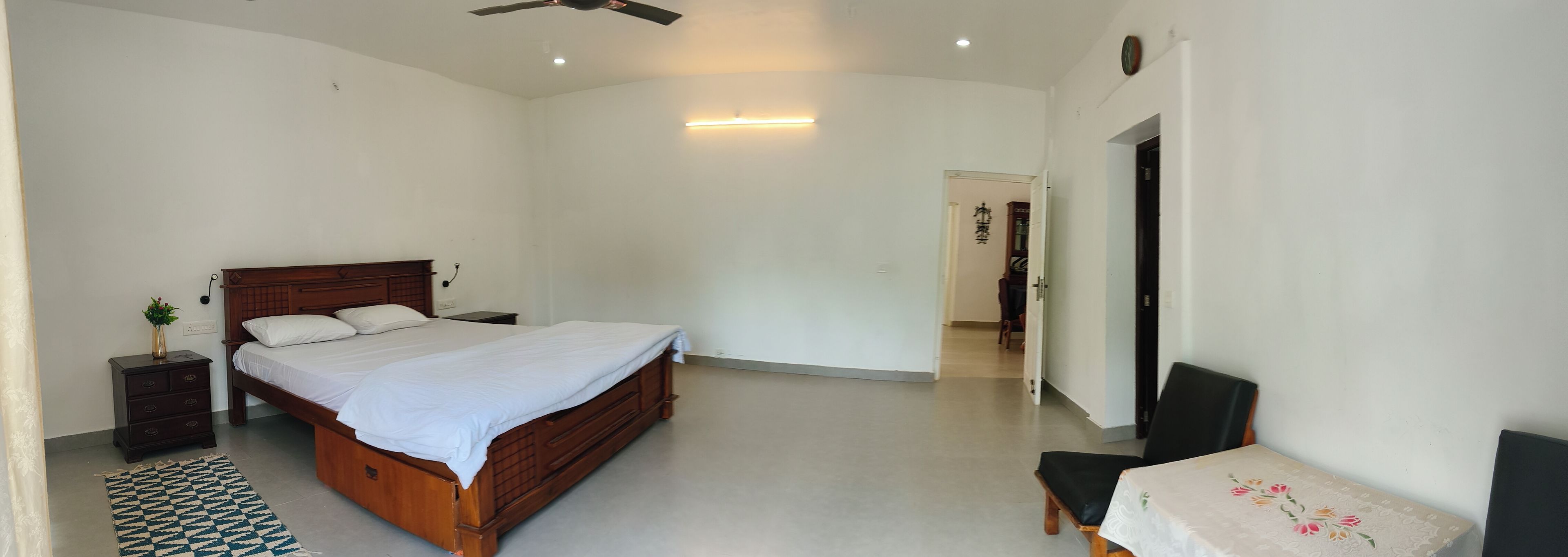 A bedroom with a wooden bed, a bedside table, a chair, and a small table with a floral tablecloth.