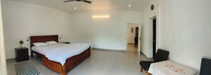 A bedroom with a wooden bed, a bedside table, a chair, and a small table with a floral tablecloth.