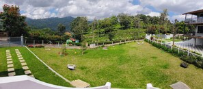A well-maintained garden with a lawn, a small seating area, and a view of a mountainous landscape. - Mighas Vila  (Full Bungalow with three Bedroom) (Yedapalli, Coonoor.)