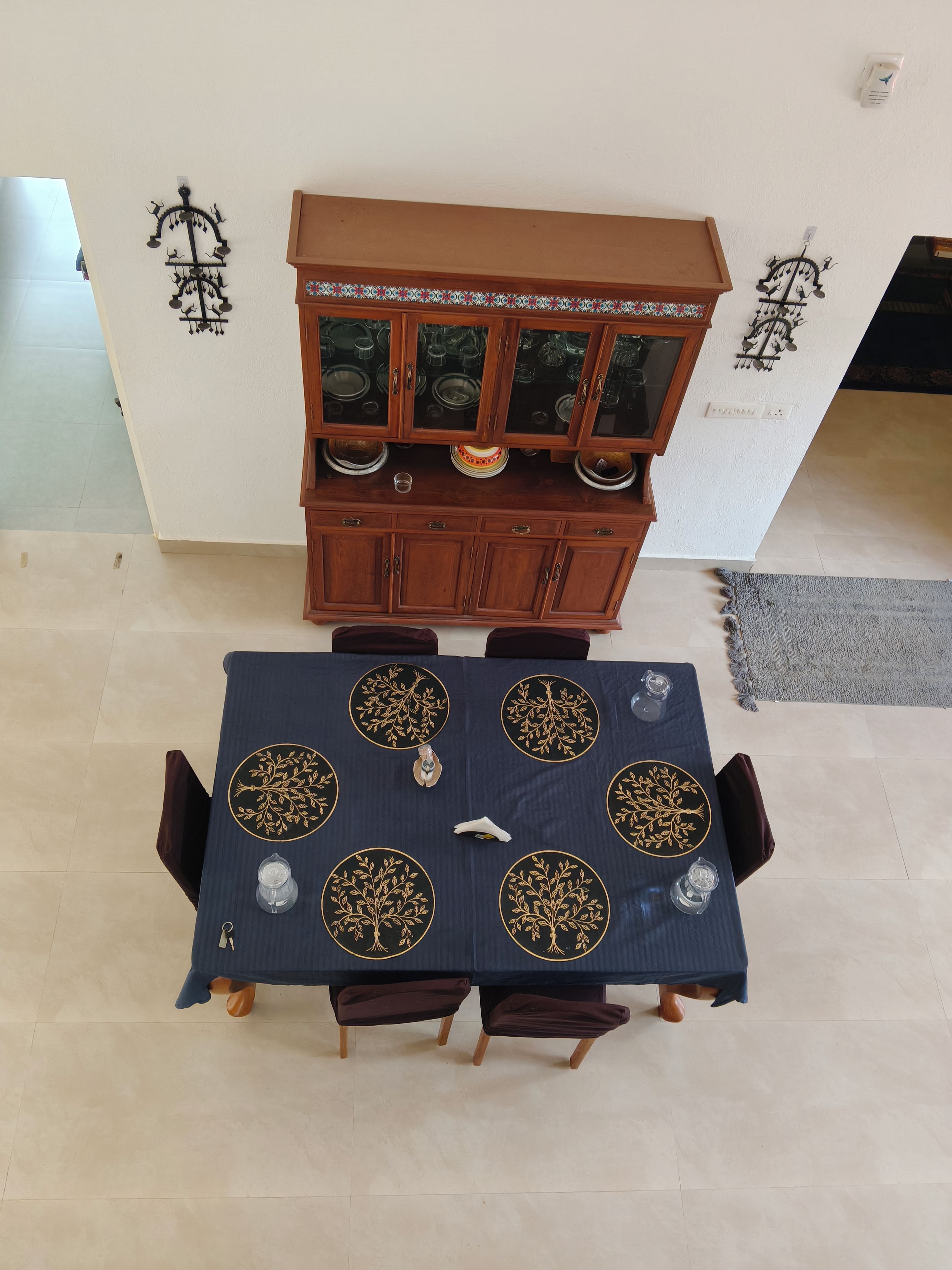 A dining table with six chairs, a cabinet above it, and a patterned tablecloth.