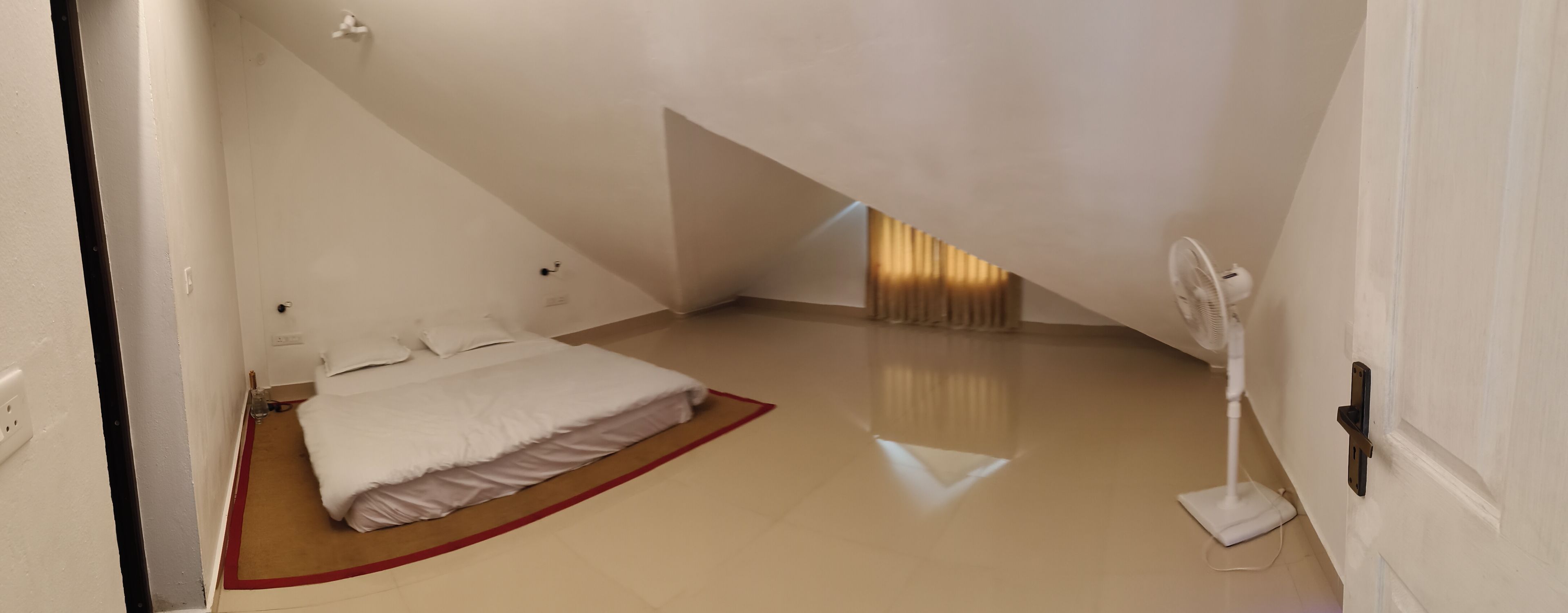 A bedroom with a bed, a red rug, a fan, and a sloped ceiling.