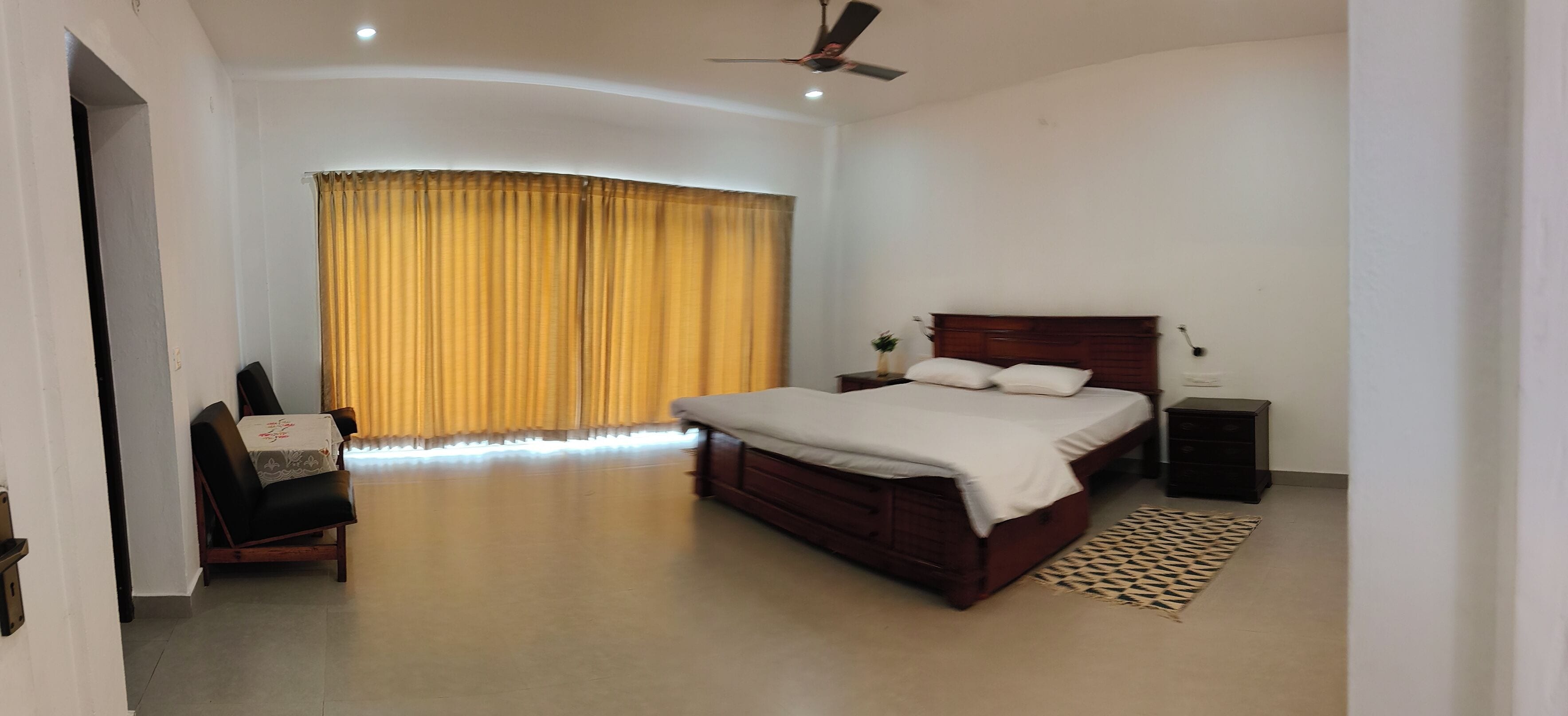 A bedroom with a bed, a nightstand, a chair, a ceiling fan, and a window with curtains.