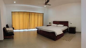 A bedroom with a bed, a nightstand, a chair, a ceiling fan, and a window with curtains.