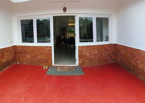 A room with a red floor, white walls, and a door leading to a dining area. - Mighas Vila  (Full Bungalow with three Bedroom) (Yedapalli, Coonoor.)