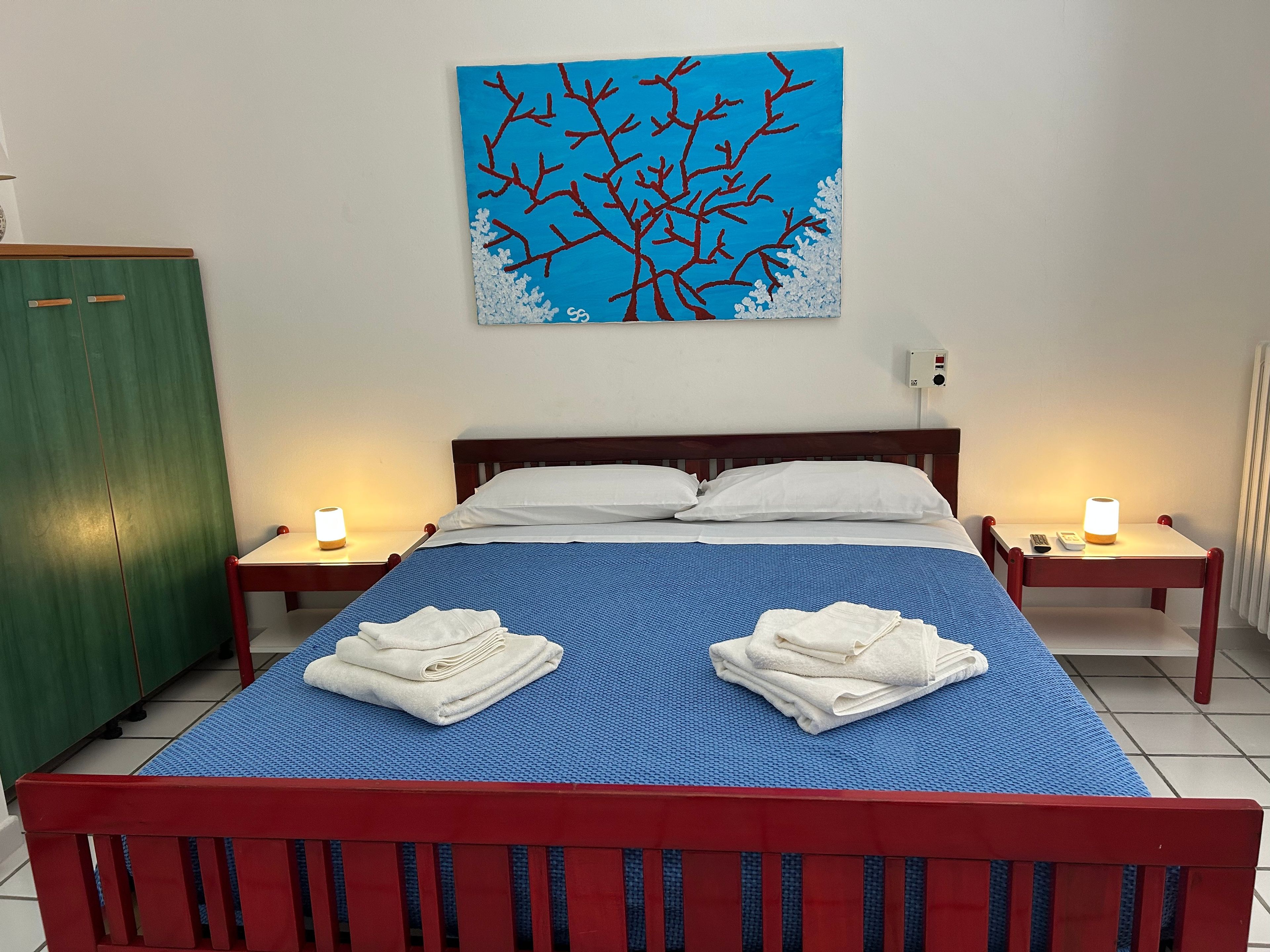 A hotel room with a bed, two nightstands, a painting, and towels on the bed.