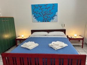 Una habitación de hotel con una cama, dos mesitas de noche, un cuadro y toallas sobre la cama.