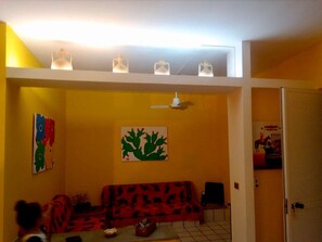 Quarto com sofá vermelho, ventoinha no teto e pintura de cactos na parede.