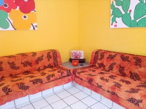 Habitació d'angle amb dos sofàs de color taronja amb dibuixos, una taula petita amb un vas vermell i dues obres d'art murals.
